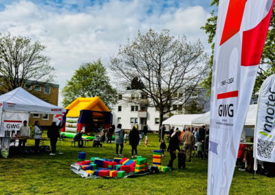 Outdoor-Gemeinschaftsfest mit Menschen, Hüpfburg, bunten Bausteinen und GWG-Bannern, die das Jubiläum 1949-2024 zeigen